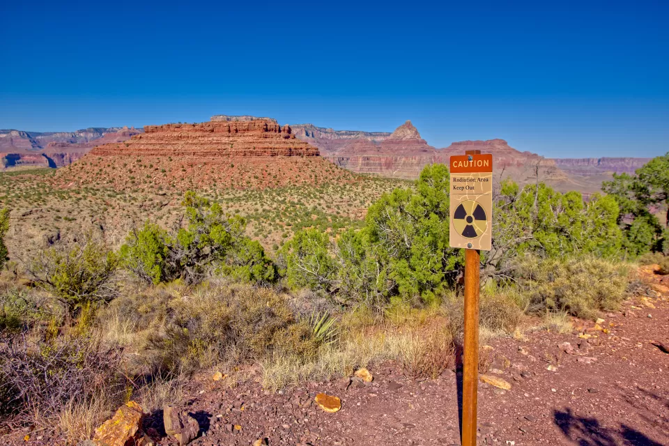 "Radiation Zone, Keep Out" sign on wood post with red Arizona desert mesa in background